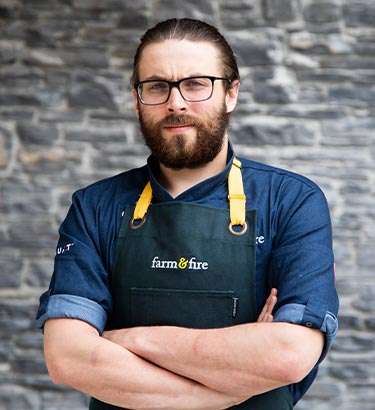 A chef stands in front of a stone wall.