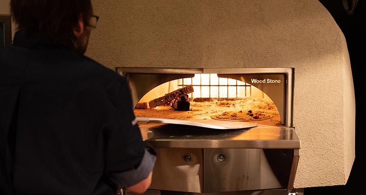 A view into a pizza oven as a chef checks on a pizza.