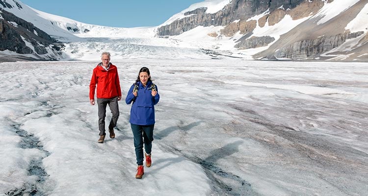 Two people walk on a glacier.