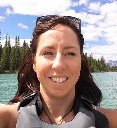 A selfie of a woman on a boat with a conifer forest behind her.