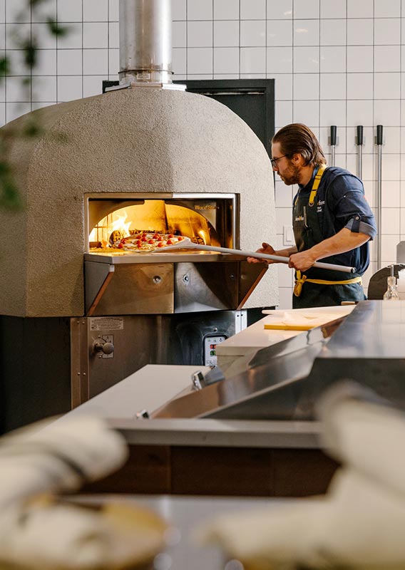 A chef puts a pizza in a large wood-fired oven.