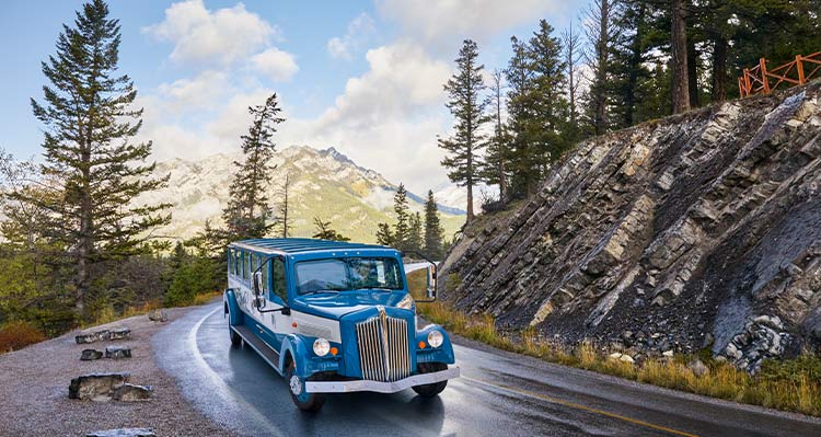 A vintage-style bus rounds a corner next to a small rocky outcropping.