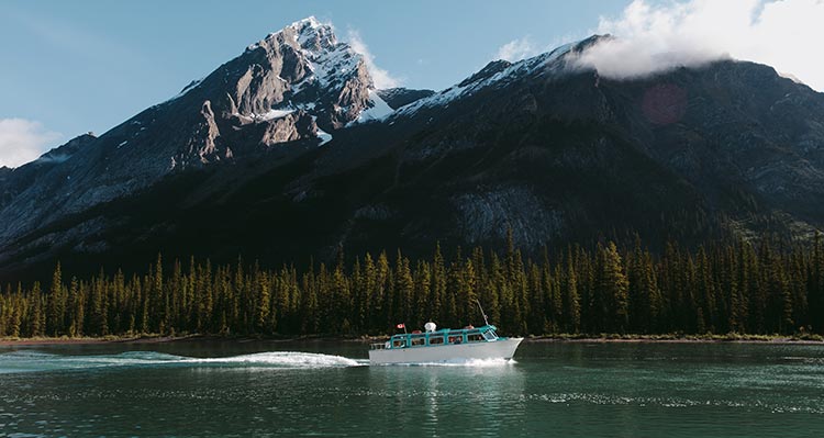 A boat cruises on a blue lake below snowy mountains.