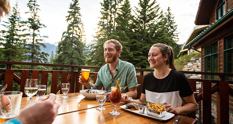 A group sits for dinner on a patio overlooking a forest.