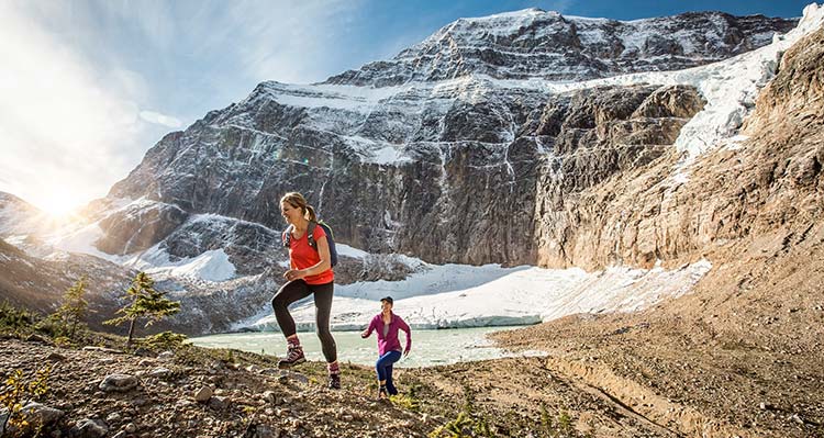 Two people hike near mountains below a glacier.