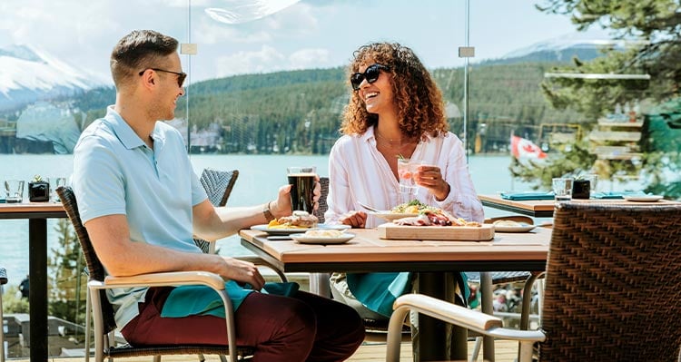 Two people sit on a patio for dinner, overlooking a lake.