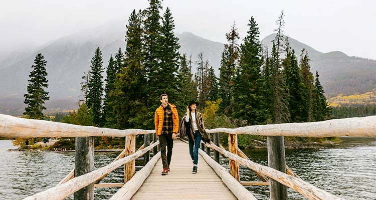 Two people walk down a small wooden bridge.