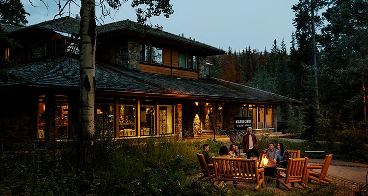 A group of people at a campfire outside of a wooden building.