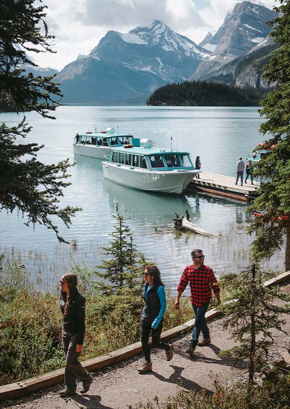 Two people are led by a tour guide along a pathway next to a lake.