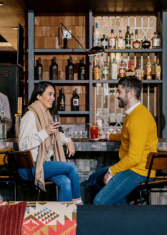 Two people sit at a restaurant bar with drinks.