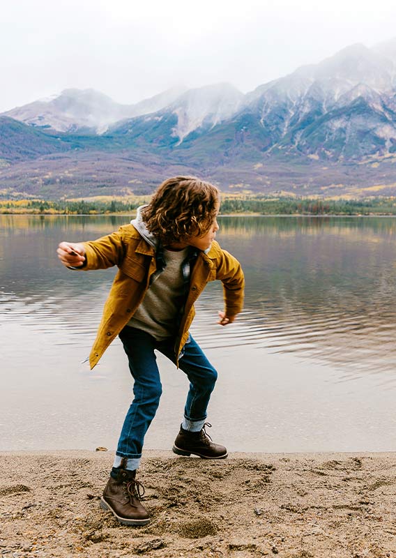 A child skips a rock from a beach onto a calm lake.
