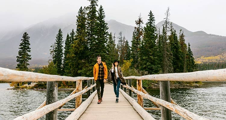 Two people walk across a wooden bridge from a small wooden island.