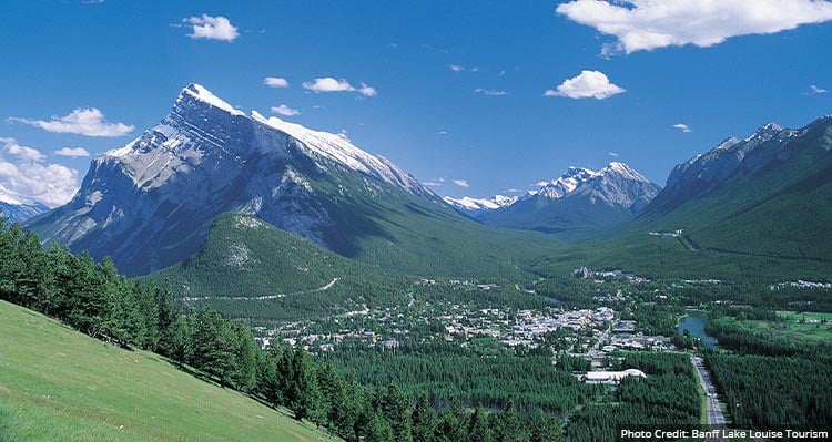 A view across a wide valley with tall snow-covered mountains all around.