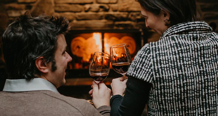 Two people sit at a fireplace.