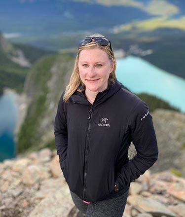 A woman stands on a viewpoint above a blue lake.