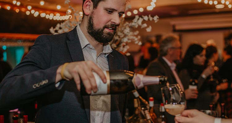 A bearded man pours a glass of champagne.