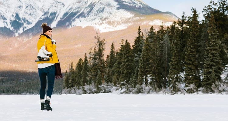 A woman stands with ice skates on a frozen lake.