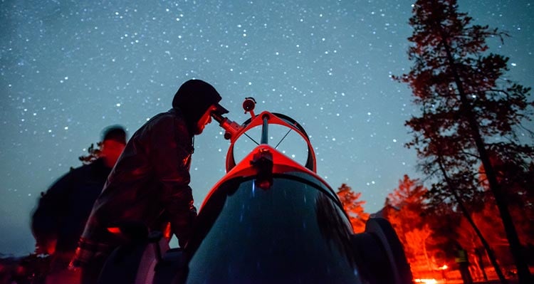 A person looks into a telescope to see the starry night sky.