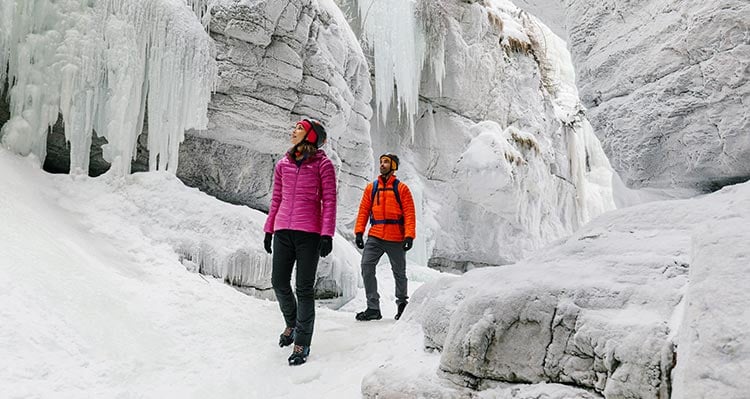 Two people walk through a frozen canyon.