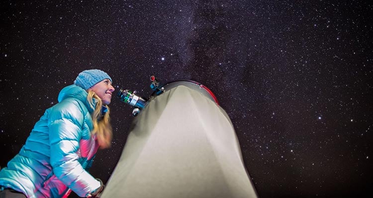 A person looks into a telescope to see the starry night sky.