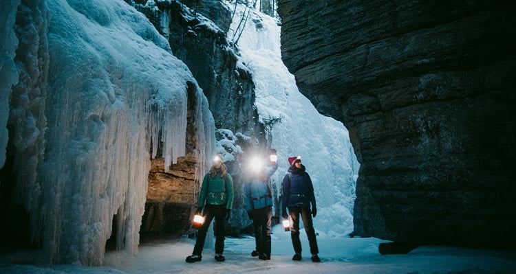 Three people stand in a frozen canyon.