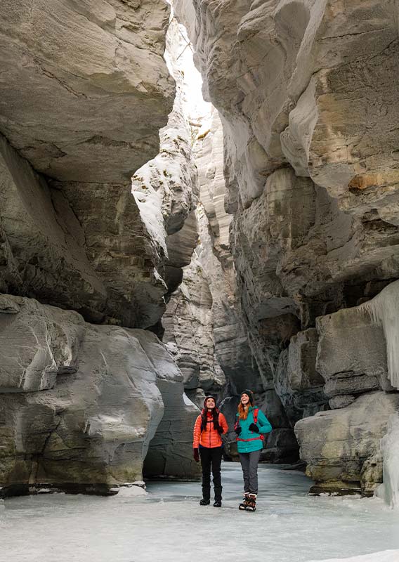 Two people walk through a frozen canyon.