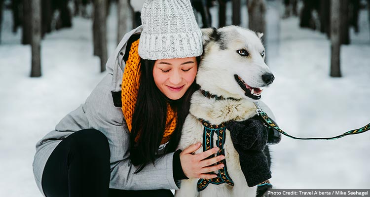 A woman bends down to hold on to her dog.