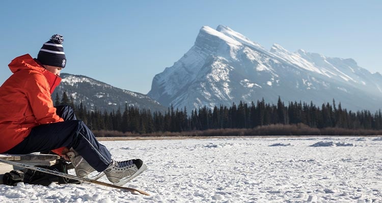 A person ties up their ice skates at the edge of a frozen lake.