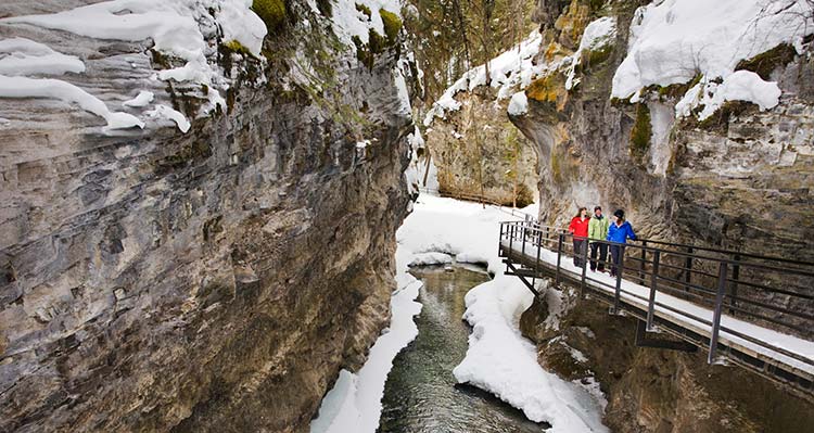 A group of people walk along a cliffside path in an icy canyon.