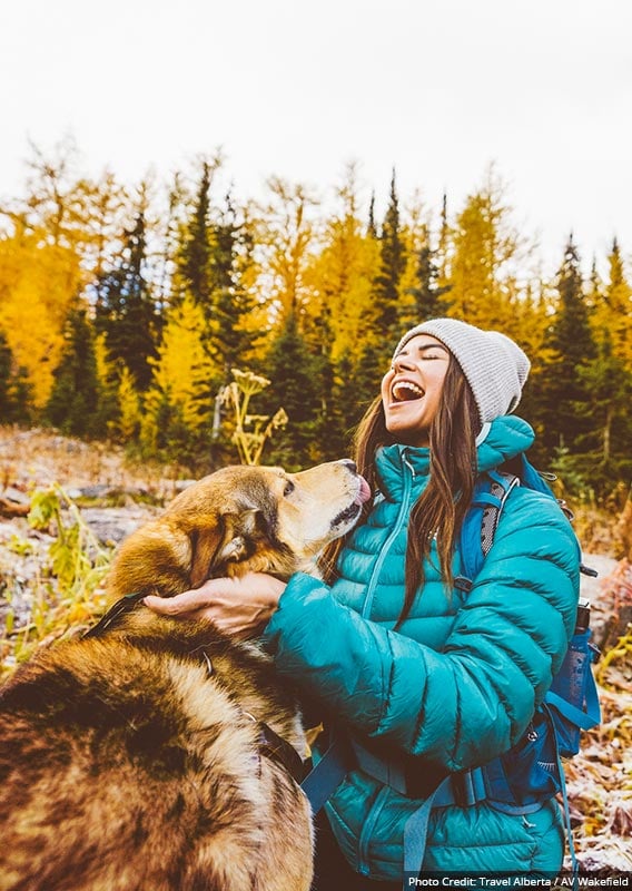 A woman laughs as her dog reaches up to her face.