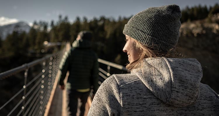 Two people walk across a long bridge stretching across a canyon.