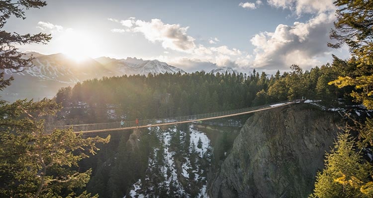 A view across a wide canyon and a narrow suspension bridge stretched across.