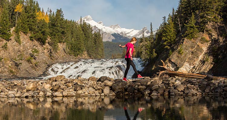 A person walks across rocks near a rushing waterfall.