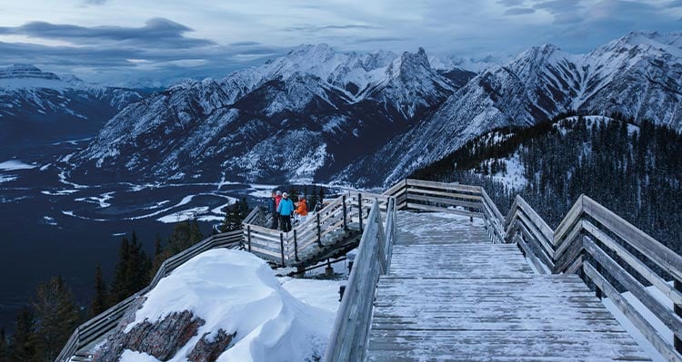 A group of friends walk along a wooden boardwalk at the top of a mountain ridge.