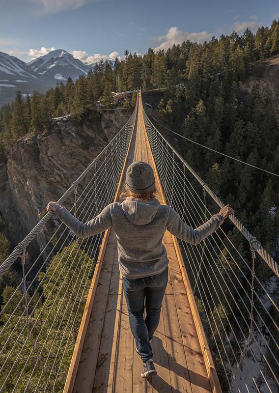 A person walks along a wooden footbridge over a deep, wide canyon.