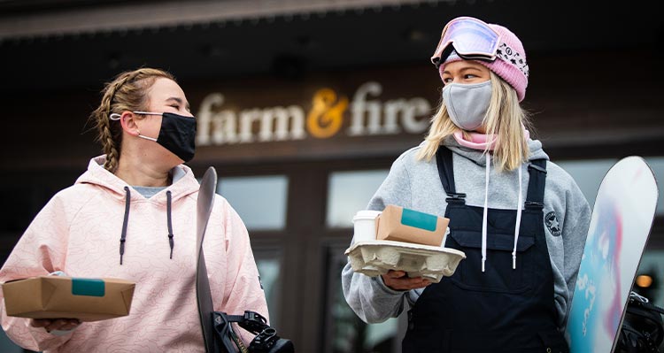 Two people walk out from a restaurant with take-out containers.