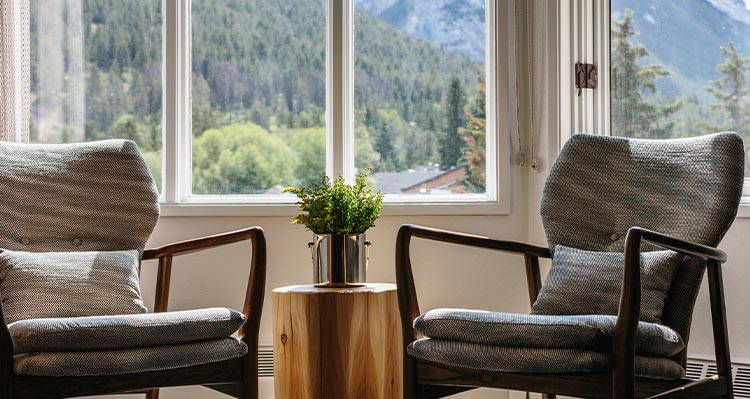 Two chairs near a large window overlooking a forest.