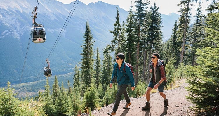 Two men hike up the path under the gondola cabins