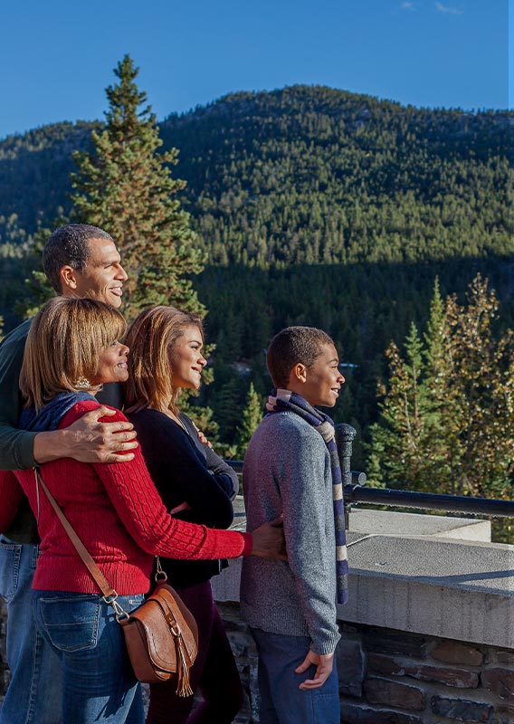 A family looks out to the landscape, standing on balcony, mountain behind