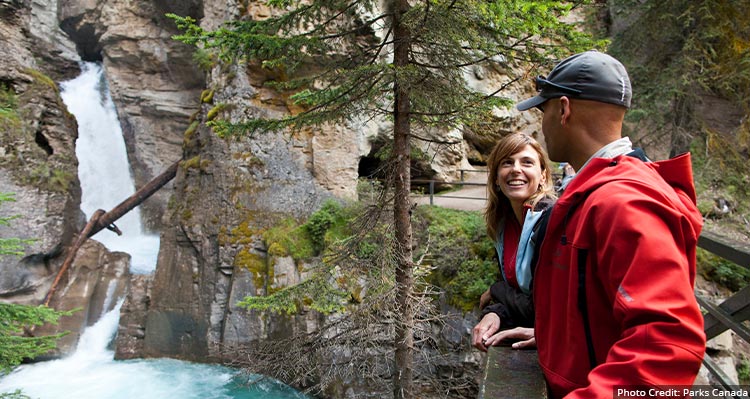 A couple stand on a bridge looking at the waterfall in the distance