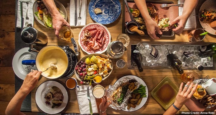 View from above a table, a group of people enjoy a large spread of food and drink.