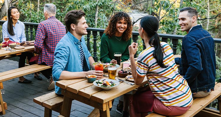 A group of friends sit at an outdoor patio table enjoying food and beverages.