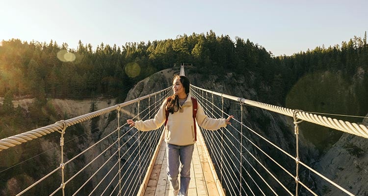 A girl crosses the suspension bridge, hands holding the railing.