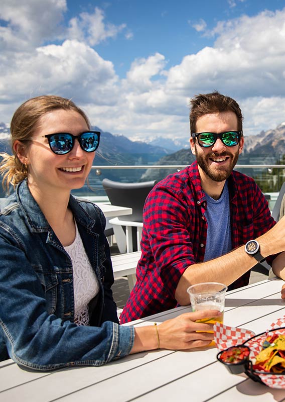 A group of friends enjoy food and a beverage at the top of a mountain.