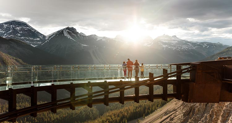 A family watches the sunset over the mountains while standing on the skywalk.