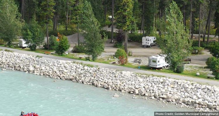 An RV park surrounded by forest and a flowing river beside.