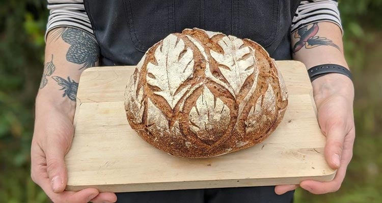 A baker showcases fresh bread on a wood cutting board.