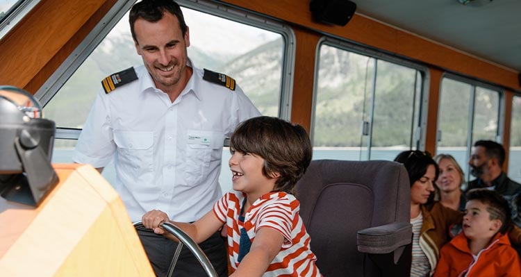 A child pretends to drive the boat while the captain stands behind.