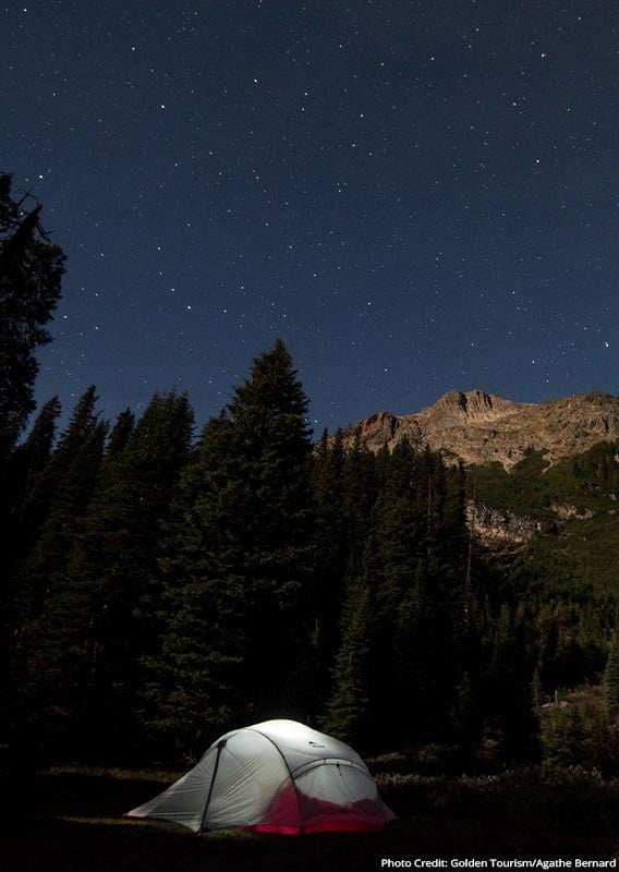 A tent is lit with a flashlight, at night under a starry sky.