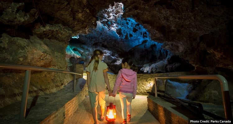 Two children walk with a lantern in their hand in the dark cave.
